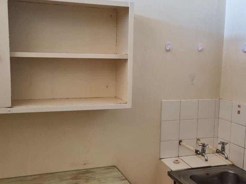 A functional laundry area featuring a stainless steel sink, tiled splashback, and built-in wall cabinetry, providing essential utility space.