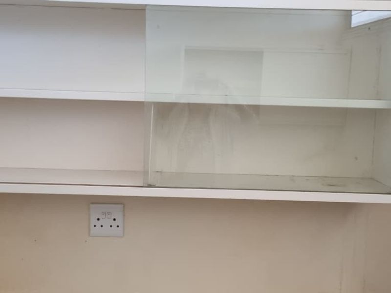 A close-up view of wall-mounted kitchen cabinetry with sliding glass doors and an integrated electrical outlet, showing signs of wear.