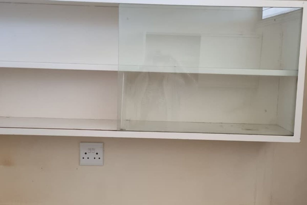 A close-up view of wall-mounted kitchen cabinetry with sliding glass doors and an integrated electrical outlet, showing signs of wear.