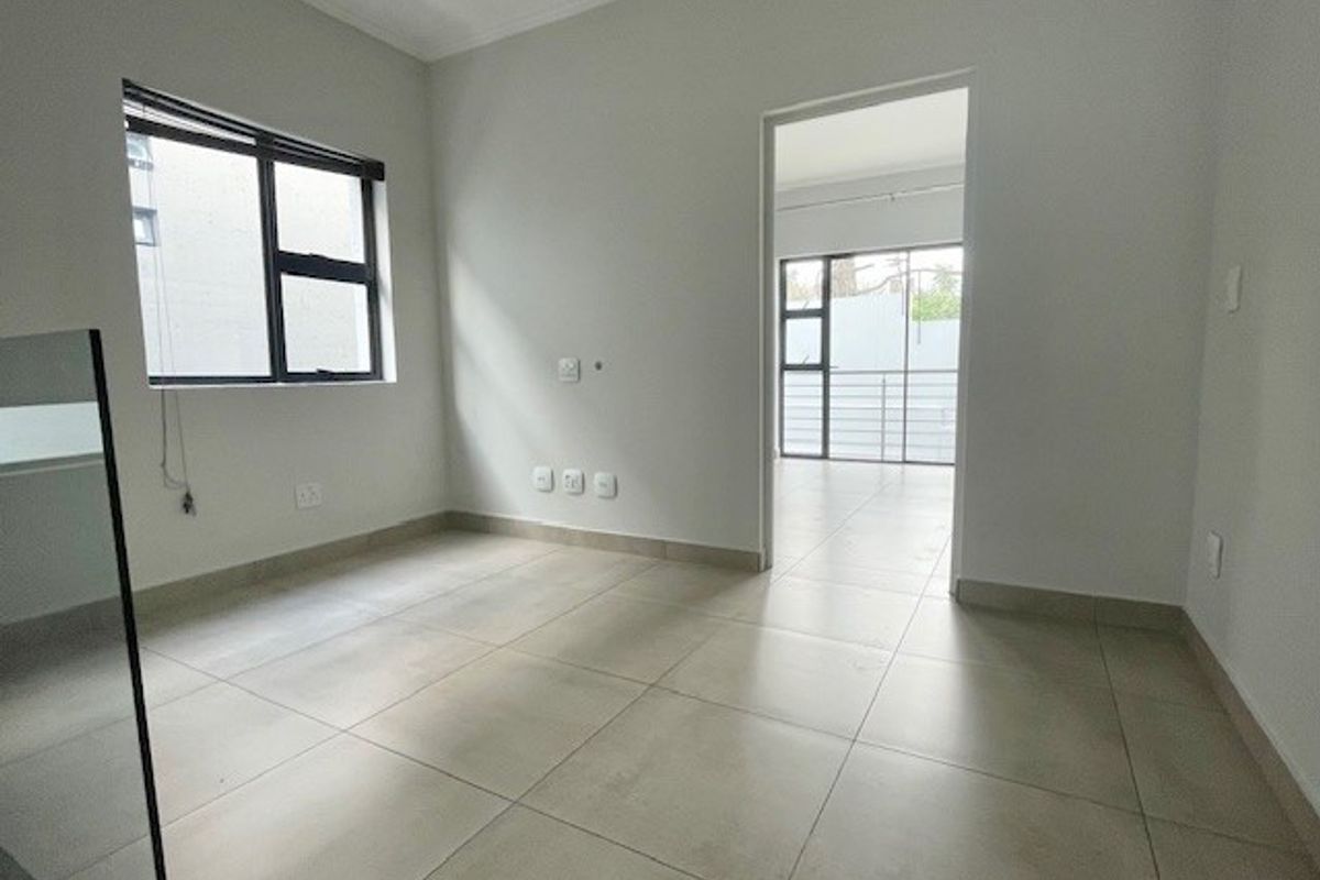 A bright, empty bedroom featuring neutral tiled flooring, modern aluminium window frames, and clean white walls, offering a versatile space for customization.