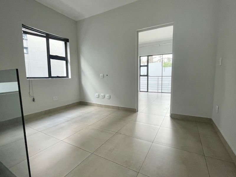 A bright, empty bedroom featuring neutral tiled flooring, modern aluminium window frames, and clean white walls, offering a versatile space for customization.