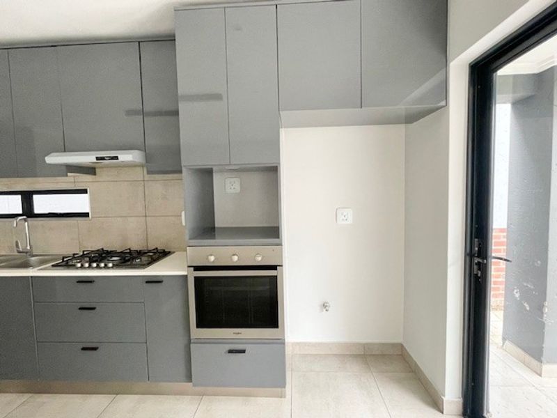 Modern kitchen featuring grey built-in cabinetry, gas hob, extractor fan, built-in oven, and tiled finishes with direct access to an outdoor area.