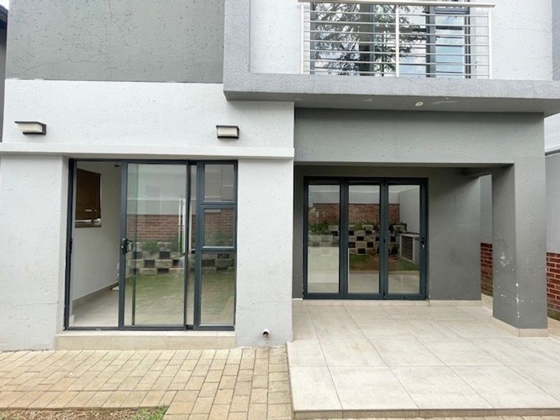 Rear exterior view featuring a paved patio, sliding glass doors, and a balcony with metal railings, set against a modern grey facade.