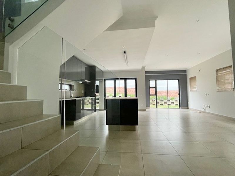 Spacious open-plan living area featuring modern tiled floors, a sleek kitchen with island, and glass staircase, leading out to the rear garden.