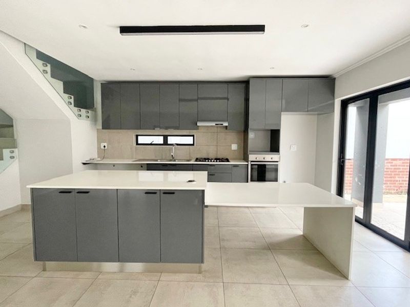 Modern kitchen featuring sleek grey cabinetry, a large central island with an integrated breakfast bar, stone countertops, and high-quality built-in appliances.