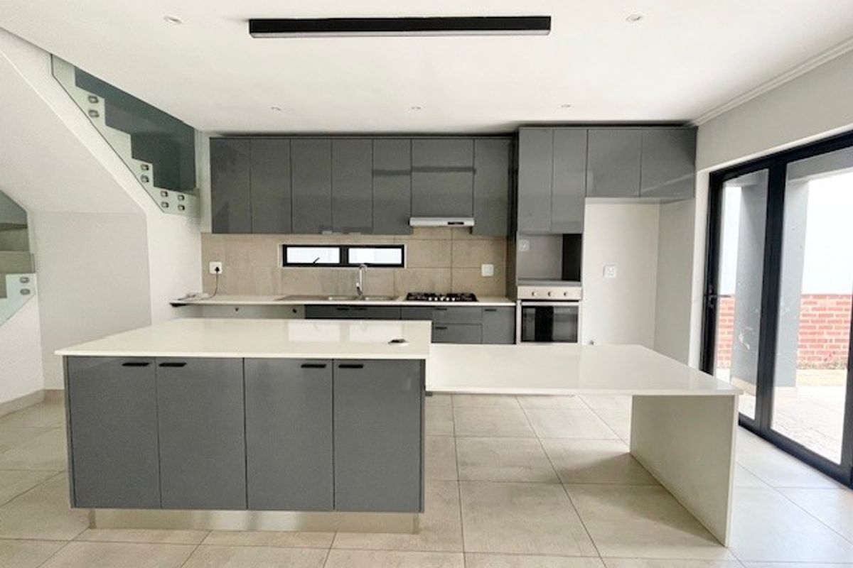 Modern kitchen featuring sleek grey cabinetry, a large central island with an integrated breakfast bar, stone countertops, and high-quality built-in appliances.