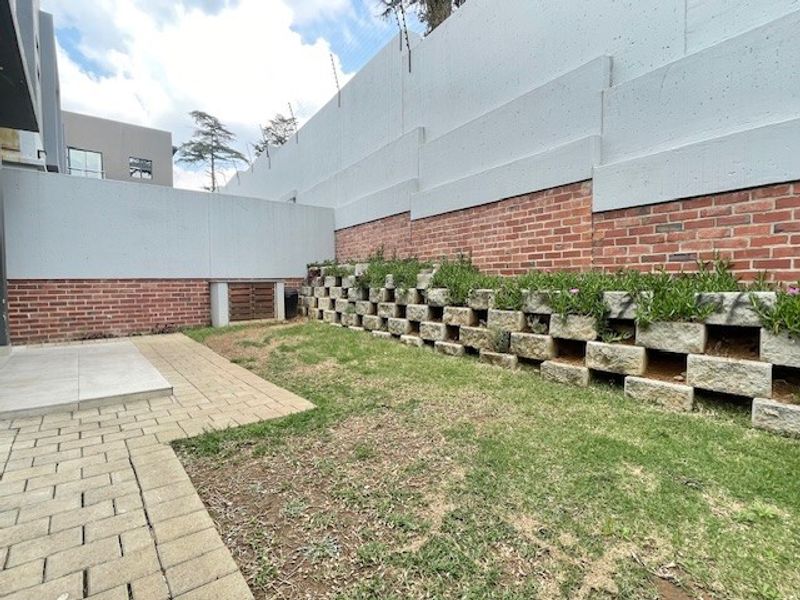 A rear garden area featuring a paved patio, a lawn, and a tiered brick and concrete retaining wall structure.
