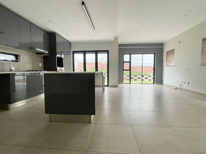 Modern open-plan kitchen and living area featuring sleek grey cabinetry, a central island, tiled floors, and large sliding doors leading to the rear garden.