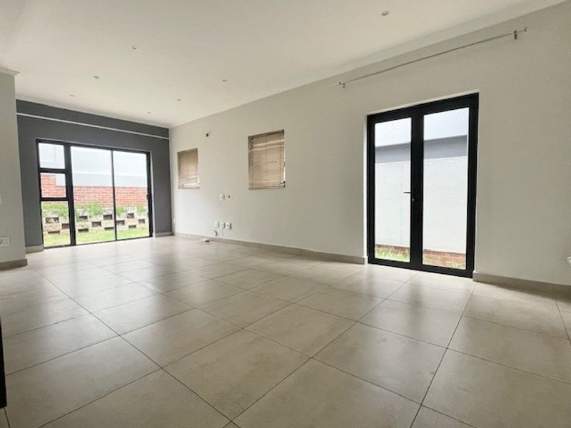 Spacious, empty living area featuring neutral tiled flooring, recessed lighting, and dual access points to the exterior through sliding and french doors.