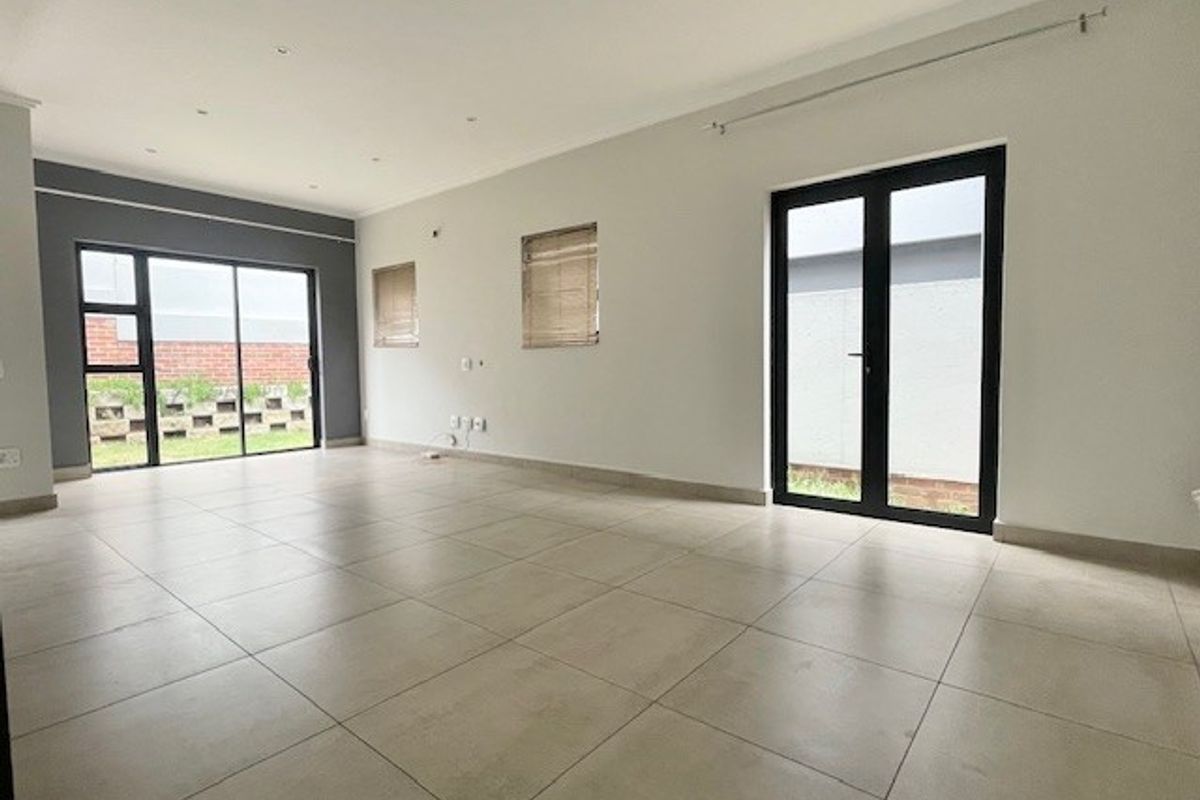 Spacious, empty living area featuring neutral tiled flooring, recessed lighting, and dual access points to the exterior through sliding and french doors.