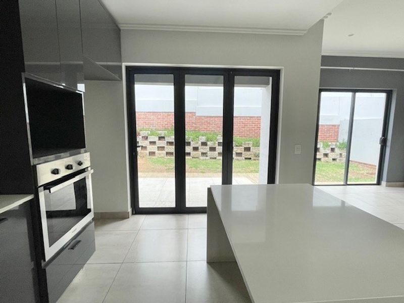 Modern kitchen featuring a central island, built-in oven, and large glass doors opening to a private rear garden area.