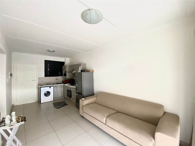 Open plan living area featuring a compact kitchen with built-in cabinetry, oven, and tiled flooring throughout the space.