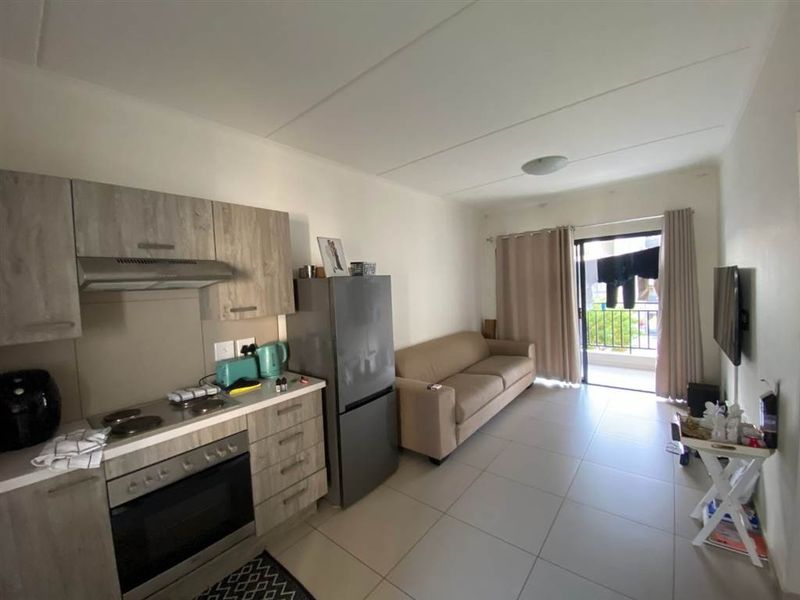 Open-plan living area featuring a modern kitchen with built-in cabinetry, electric hob, and oven, flowing seamlessly to a private balcony.