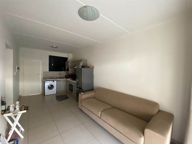Open plan living area featuring a compact kitchen with built-in cabinetry, oven, and extractor fan, finished with neutral floor tiles throughout.