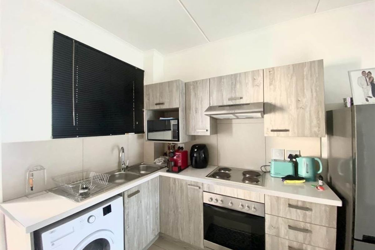 Compact kitchen featuring modern wood-look cabinetry, built-in oven, electric hob, extractor fan, and a double bowl sink with integrated laundry appliance space.