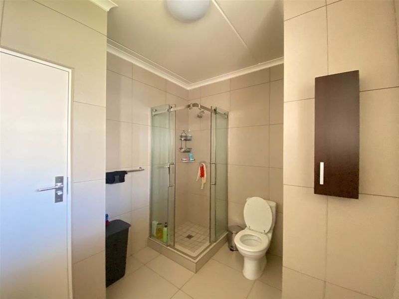 A functional bathroom featuring a glass shower enclosure, neutral ceramic wall and floor tiling, and a wall-mounted storage cabinet.