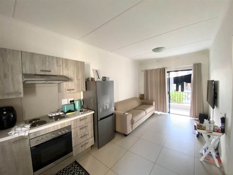 An open-plan living area featuring a modern kitchen with built-in cabinetry, electric hob, and oven, leading to a balcony through a sliding glass door.