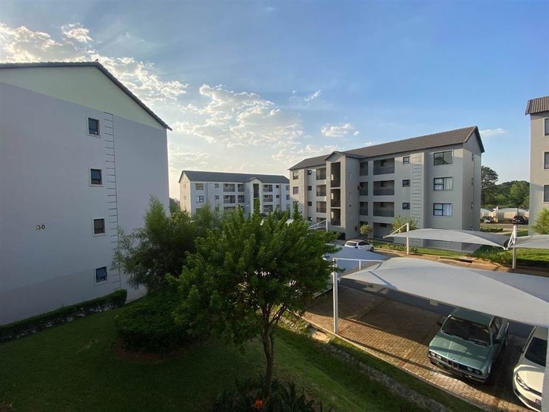 View of the apartment complex grounds featuring paved parking with shade cloth carports, landscaped garden areas, and multi-story residential buildings.