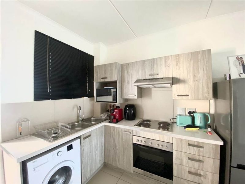 Compact kitchen featuring modern wood-look cabinetry, built-in oven, electric hob, extractor fan, and a double bowl sink with integrated laundry appliance space.