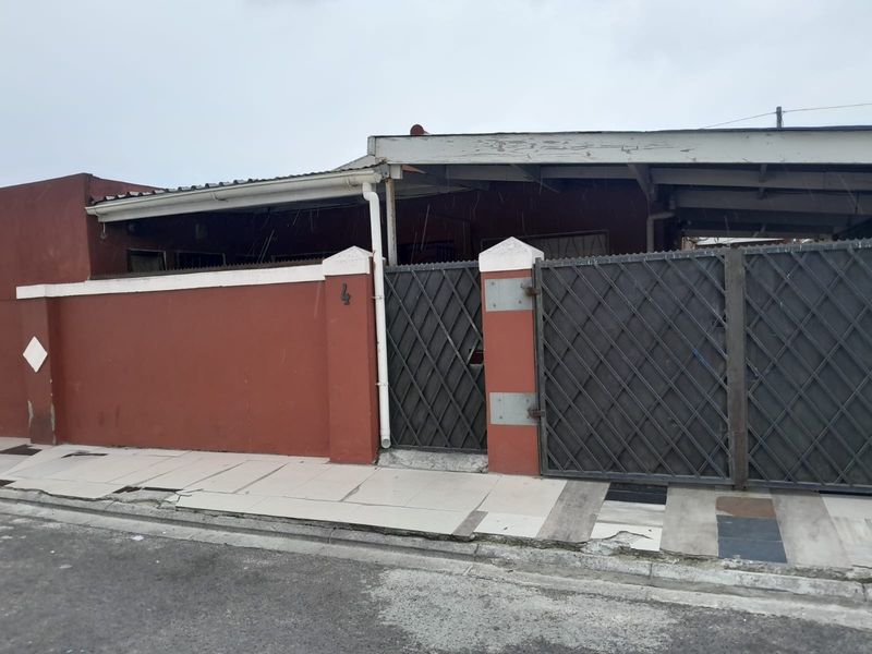 Front exterior view of the property featuring a boundary wall, metal security gate, and a covered carport area with paved frontage.