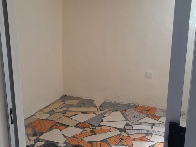 An empty room featuring a mosaic-style tiled floor, plain walls, and basic electrical fixtures, requiring renovation to improve the flooring and overall finish.