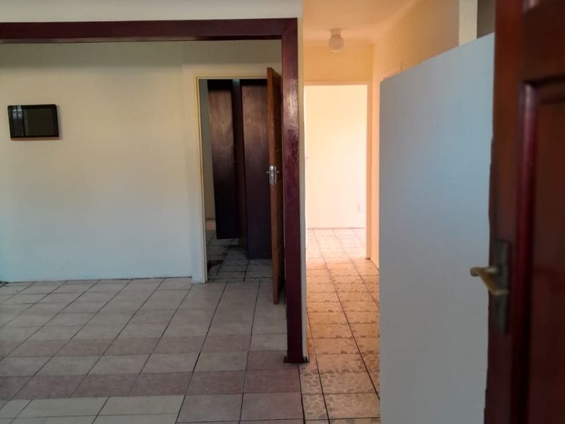 An empty interior hallway featuring ceramic tiled flooring and timber door frames, leading into adjacent rooms with built-in storage.