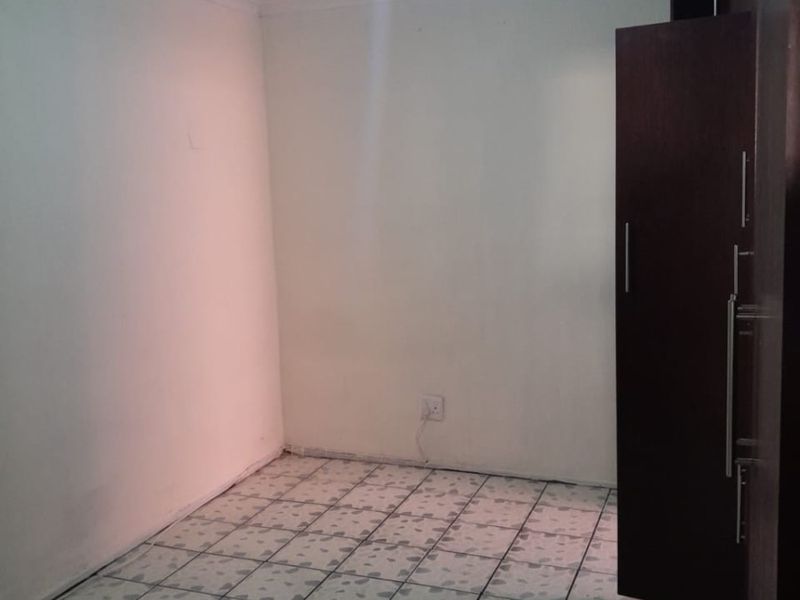 A simple, empty bedroom featuring tiled flooring and a built-in cupboard, providing a blank canvas for personalization.