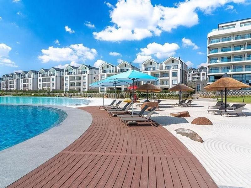 A well-maintained communal pool area featuring a swimming pool, timber decking, and a sandy beach section within a modern apartment complex.