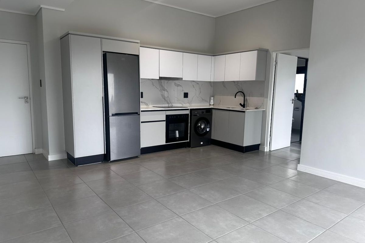 Modern open-plan kitchen featuring sleek white cabinetry, marble-look splashback, integrated appliances, and neutral tiled flooring in a clean, contemporary apartment setting.