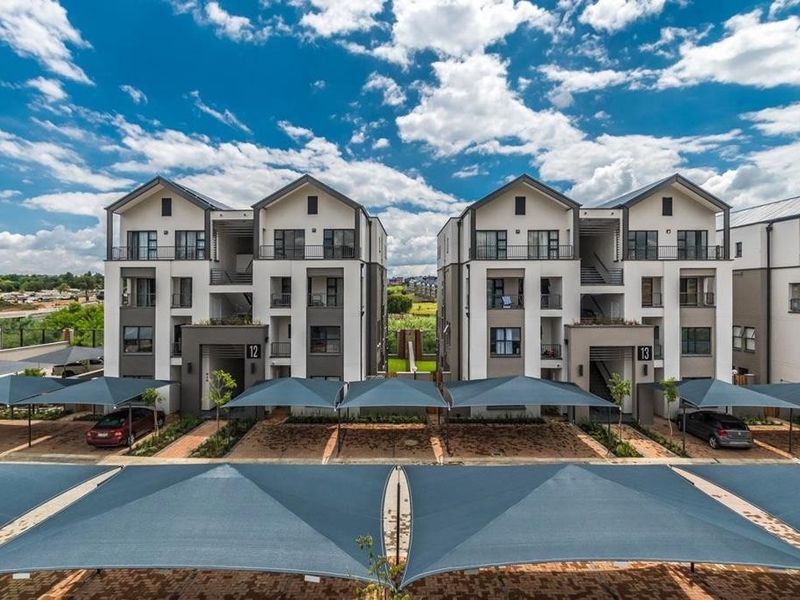 Aerial view of a modern apartment complex featuring multi-story units with private balconies and dedicated shade cloth parking bays.