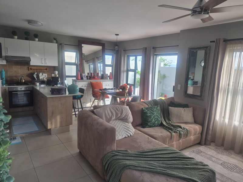 Open-plan living area featuring a modern kitchen with built-in cabinetry, gas hob, and oven, flowing into a comfortable lounge with access to the patio.