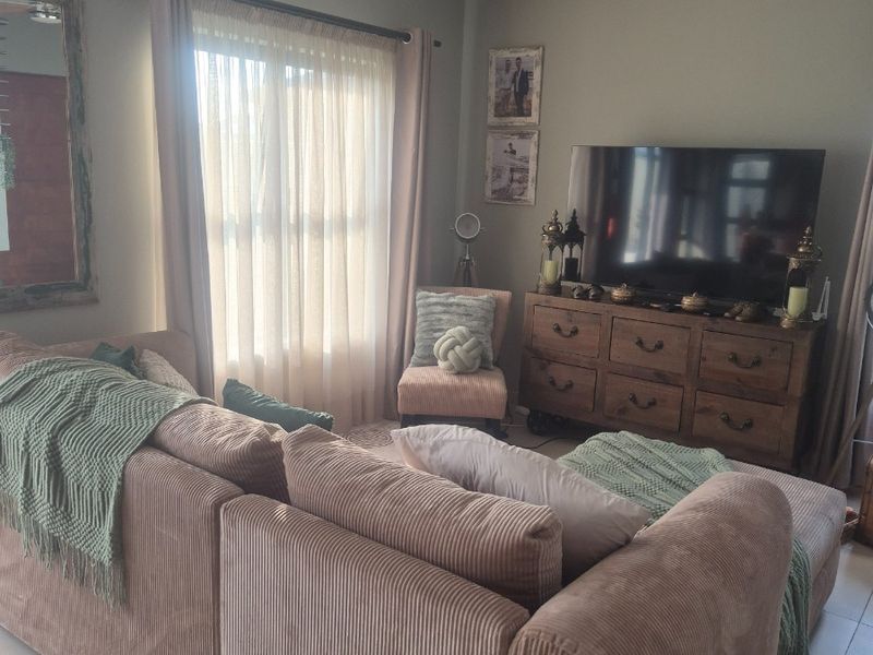 A comfortable living room featuring tiled flooring, a ceiling fan, and natural light through large windows with curtain rails.