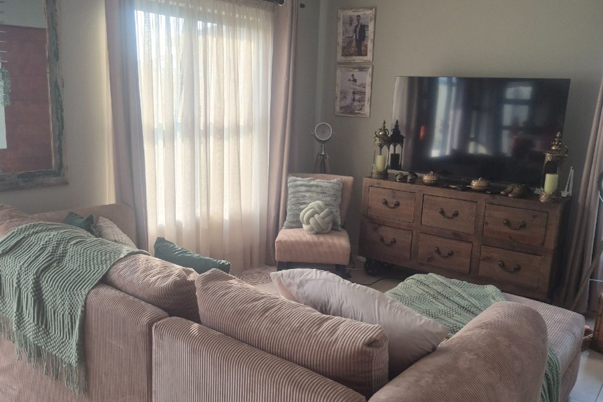 A comfortable living room featuring tiled flooring, a ceiling fan, and natural light through large windows with curtain rails.