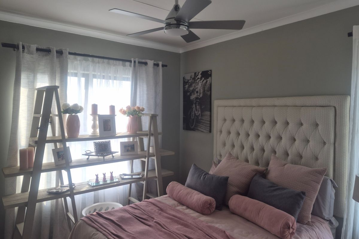 A well-maintained bedroom featuring a modern ceiling fan, neutral wall tones, and a large window with fitted curtain rods.