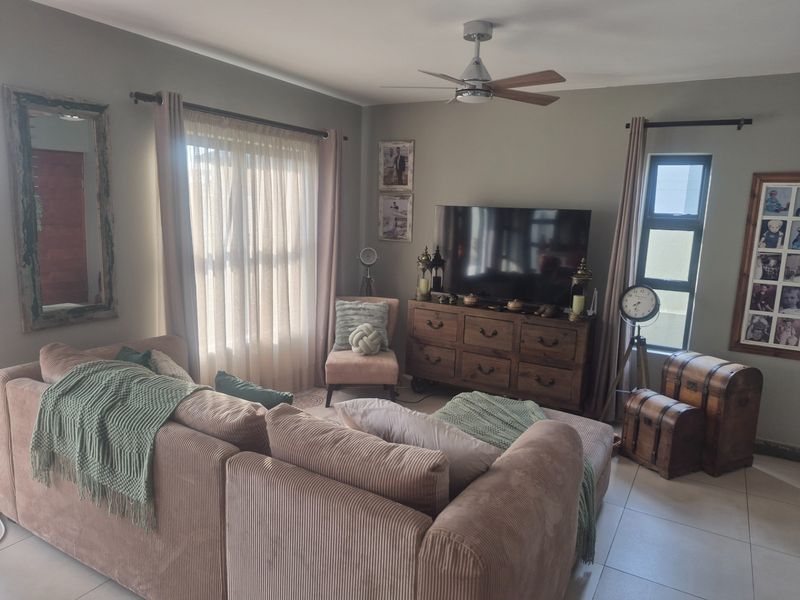 A comfortable living room featuring tiled flooring, a ceiling fan, and large windows that provide natural light.