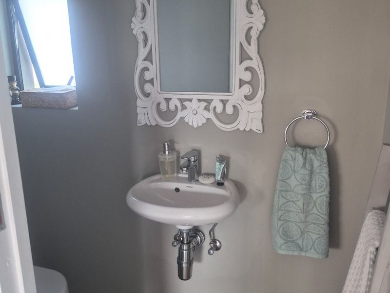 A compact guest bathroom featuring a wall-mounted basin, chrome fixtures, and a toilet, finished with neutral wall tones and tiled flooring.