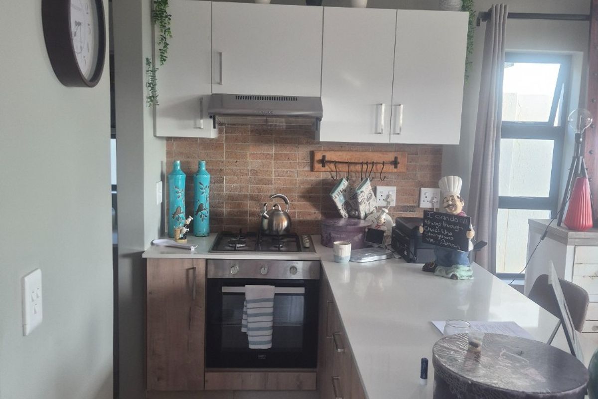 A compact, modern kitchen featuring light wood-finish cabinetry, stone countertops, a built-in oven with gas hob, and a decorative tiled backsplash.
