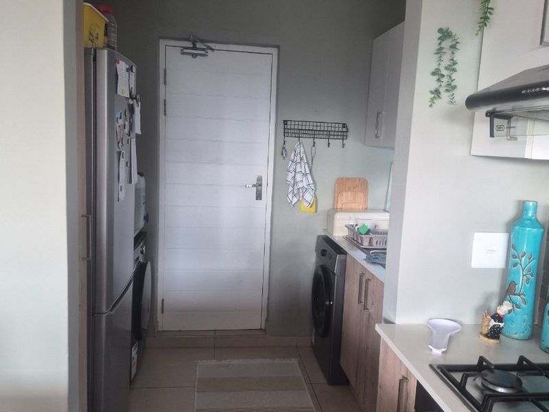A functional scullery area featuring built-in cabinetry, a gas hob with extractor fan, and tiled flooring, providing convenient additional workspace and laundry access.