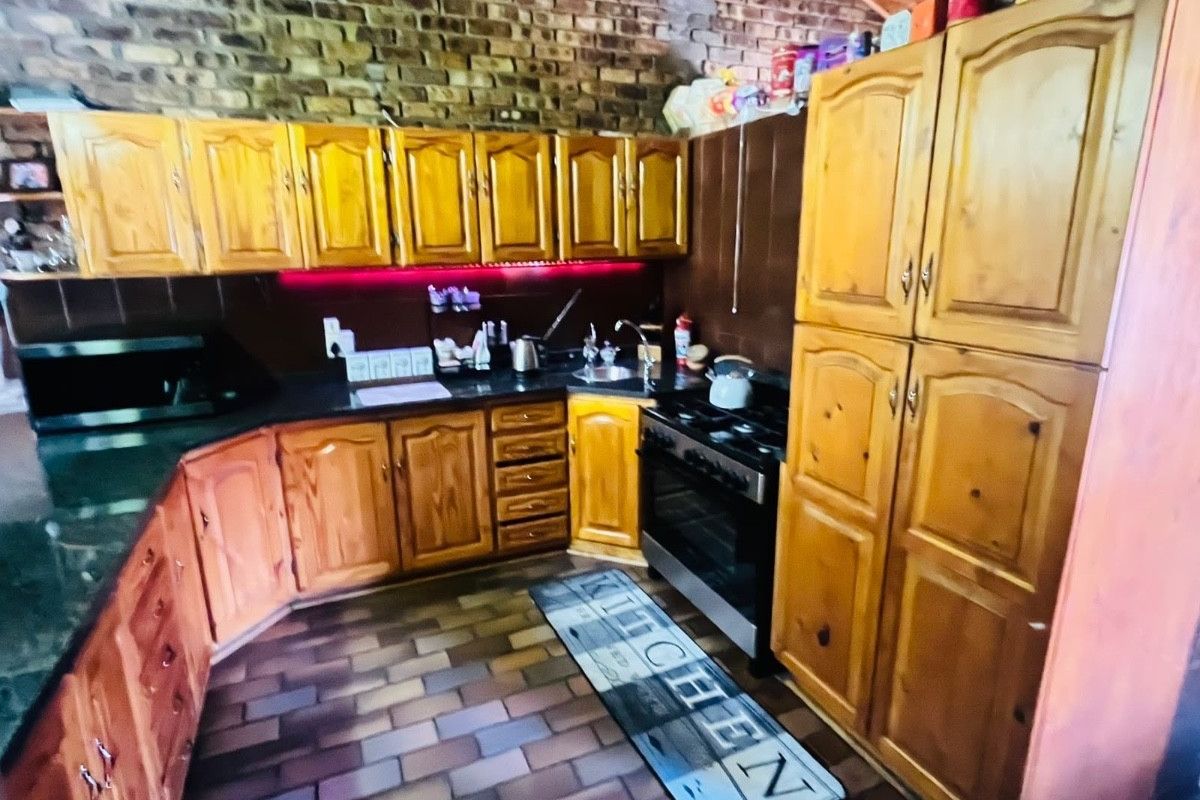 A rustic kitchen featuring exposed brick walls, timber cabinetry, and a vaulted timber ceiling with tiled flooring.