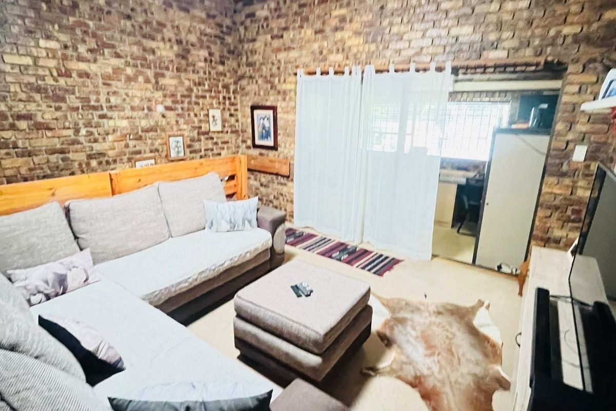 Living room featuring rustic exposed brick walls and exposed timber ceiling beams, with a sliding glass door providing access to the adjacent space.
