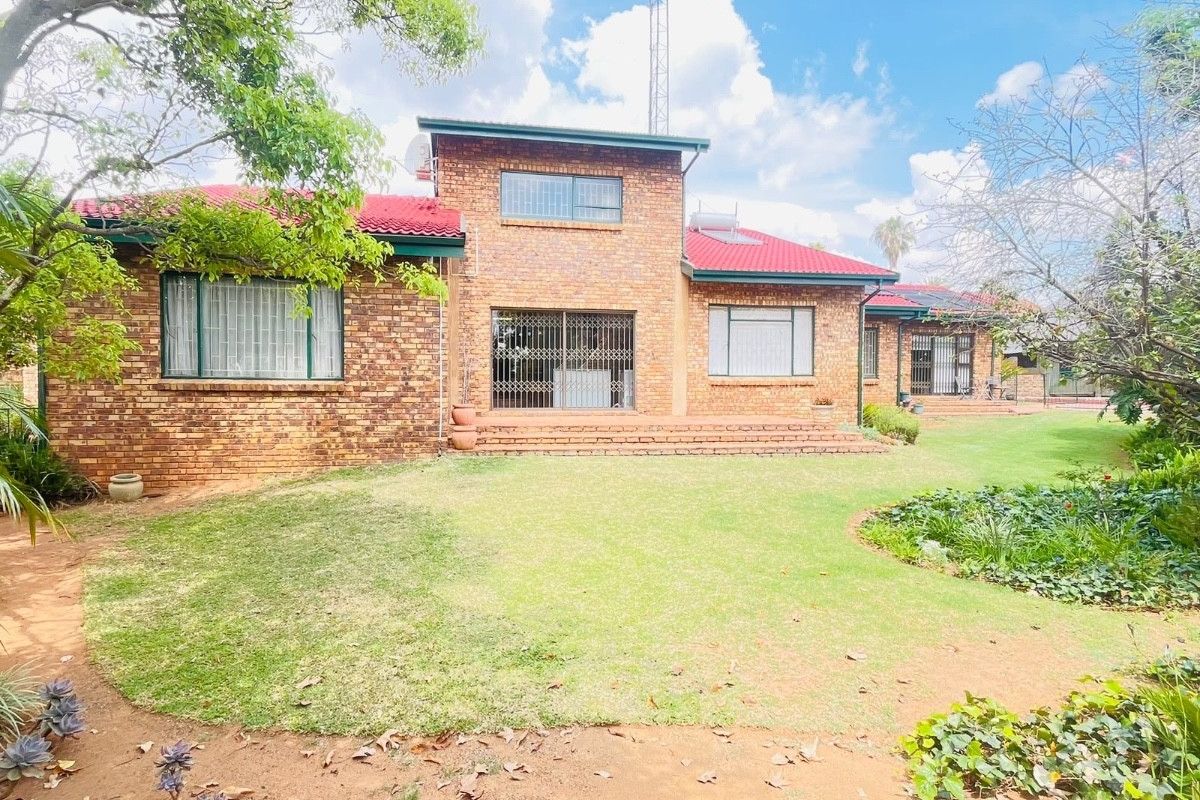 A rear view of a face brick house featuring a red metal roof, security gates, and a well-maintained garden area.