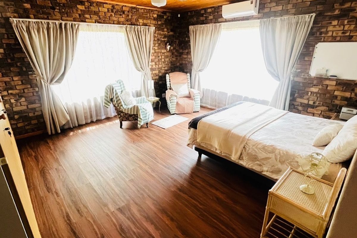 Spacious bedroom featuring exposed brick walls, timber ceiling, laminate flooring, and a split-system air conditioner.