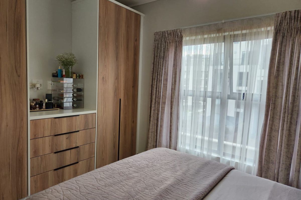 A well-maintained bedroom featuring modern wood-finish built-in cupboards and drawers, providing ample storage space and natural light through the window.
