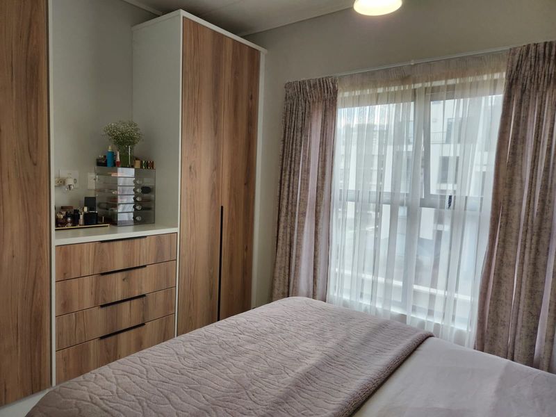 A well-maintained bedroom featuring modern wood-finish built-in cupboards and drawers, providing ample storage space and natural light through the window.