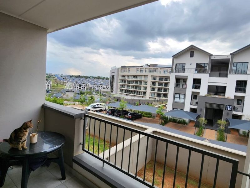 A covered balcony featuring tiled flooring and a metal balustrade, offering an elevated view of the surrounding apartment complex and parking area.