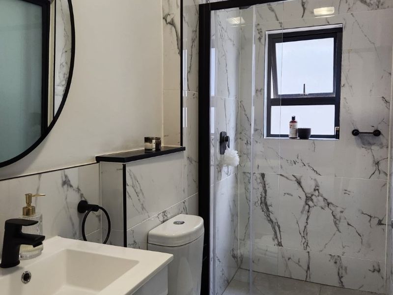Modern bathroom featuring marble-look wall tiles, a glass shower enclosure with black framing, a sleek vanity cabinet, and contemporary black fixtures.