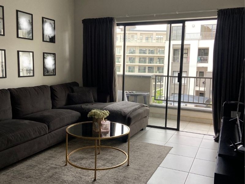 A well-maintained living room featuring tiled flooring, modern track lighting, and a large sliding glass door providing access to a private balcony.