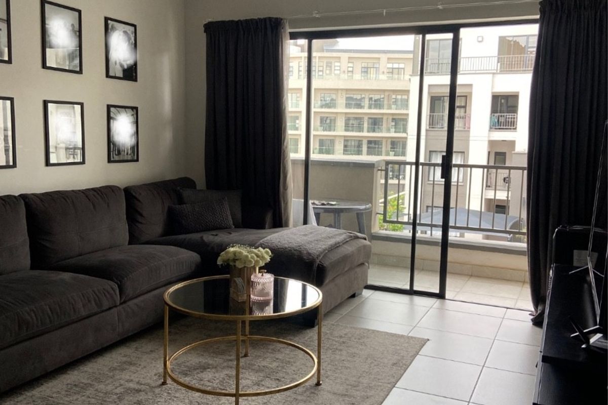 A well-maintained living room featuring tiled flooring, modern track lighting, and a large sliding glass door providing access to a private balcony.
