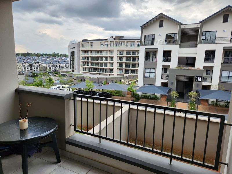 A covered balcony with a metal balustrade, offering an elevated view of the surrounding apartment complex and parking area.