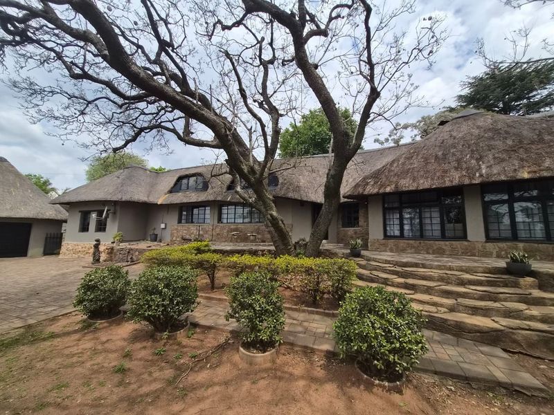 A charming single-story home featuring a traditional thatched roof, stone facade, and stone-stepped entrance surrounded by established garden landscaping.